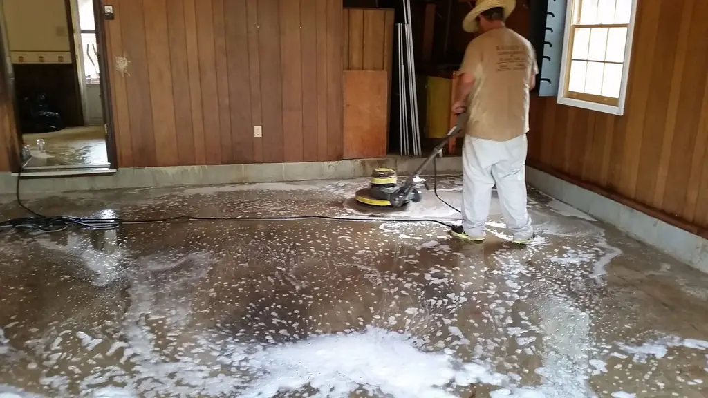 A Rainey's crew member running a floor machine across a foamed concrete floor in a wood-panelled room