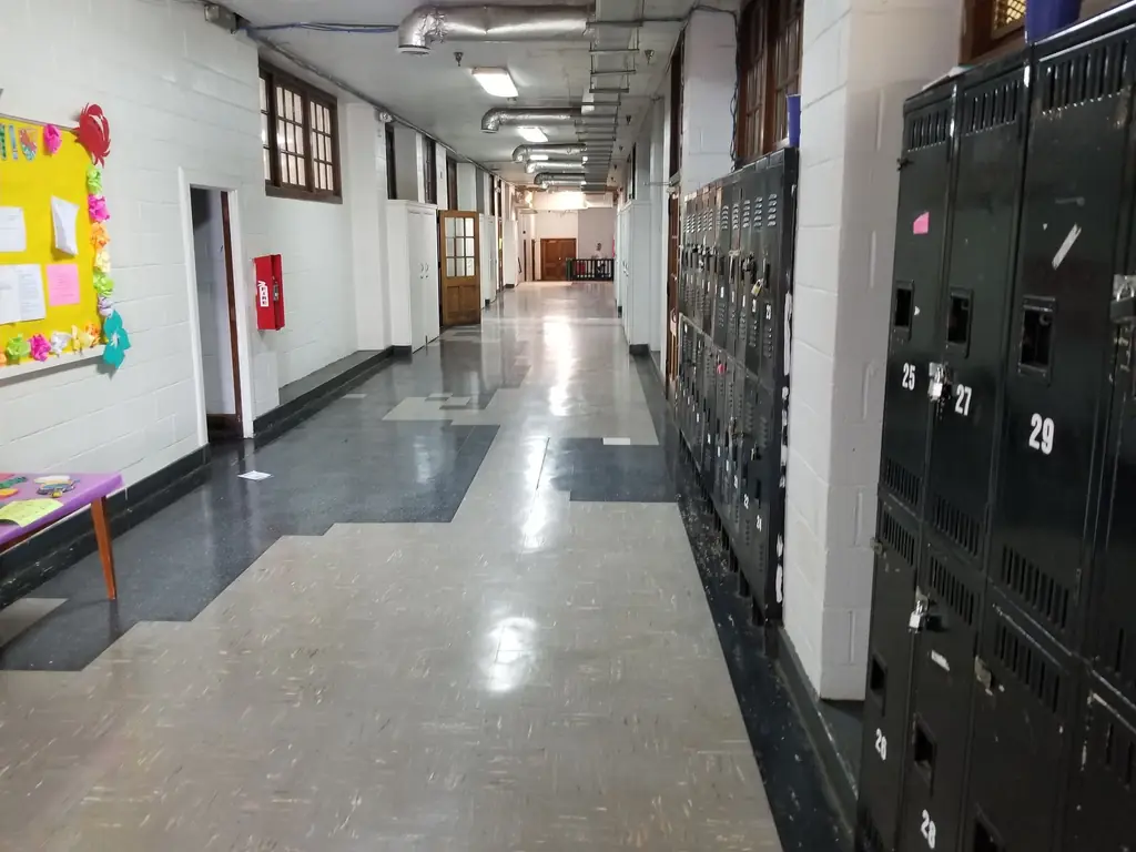 A school corridor with lockers and a maintained hard floor reflecting the overhead lighting